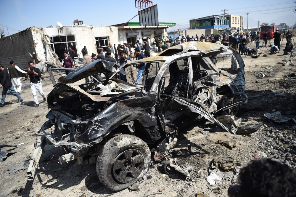 Afghan security personnel and civilians gather next to a damaged car at the site of a car bomb attack in Kabul on March 17, 2018. AFP / WAKIL KOHSAR
