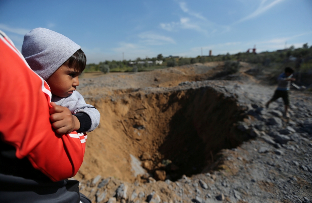 A Palestinian boy is carried as he looks at the scene of an Israeli air strike, south of Gaza City March 18, 2018. REUTERS/Ibraheem Abu Mustafa