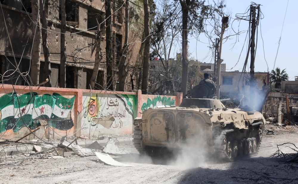  A member of the Syrian government forces rides on top of an infantry-fighting vehicle (IFV) past a mural of the flag of the Syrian opposition and writing supporting Faylaq al-Rahman (Rahman Legion), in the town of Jisreen in the southern Eastern Ghouta, 