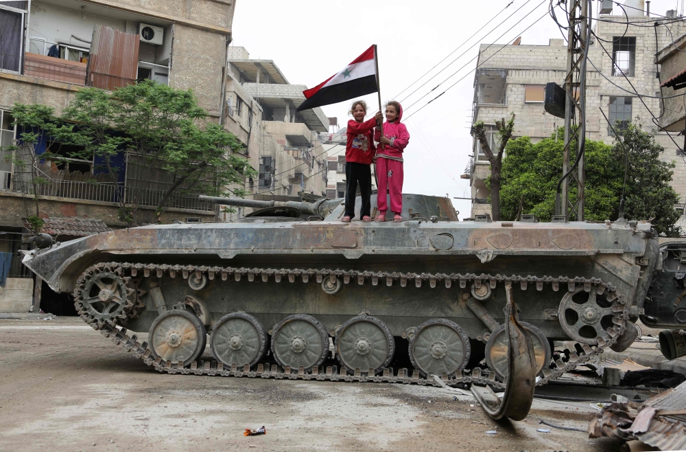 Syrian children hold a national flag while standing atop an infantry fighting vehicle (IFV) in the Eastern Ghouta town of Hazzeh on the outskirts of the Syrian capital Damascus, on March 28, 2018. / AFP / STRINGER
