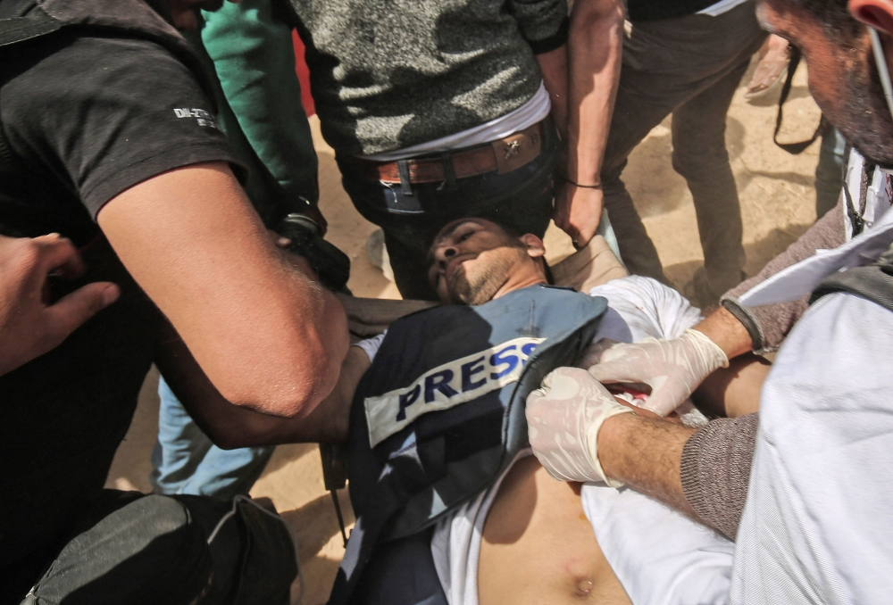 Demonstrators assist an injured Palestinian journalist Yasser Murtaja during clashes with Israeli security forces following a protest near the border with Israel, east of Khan Yunis, in the southern Gaza Strip, on April 6, 2018. AFP / SAID KHATIB