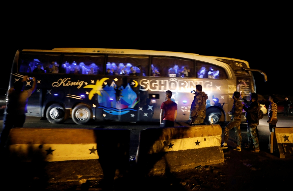 People and members of Syrian forces of President Bashar al Assad take pictures as a bus carrying freed hostages and rebels who were evacuated from the rebel-held city of Douma drives at Wafideen camp in Damascus, Syria April 8, 2018. Picture taken April 8