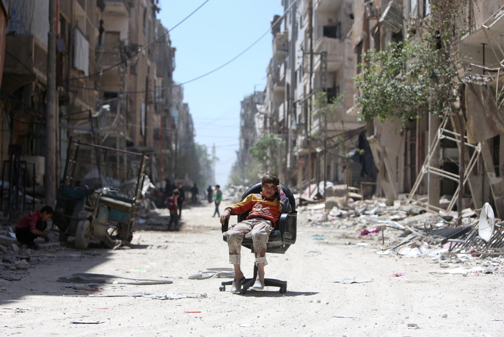 A boy sits on a chair along a damaged street at the city of Douma in Damascus, Syria April 16, 2018. REUTERS/Ali Hashisho