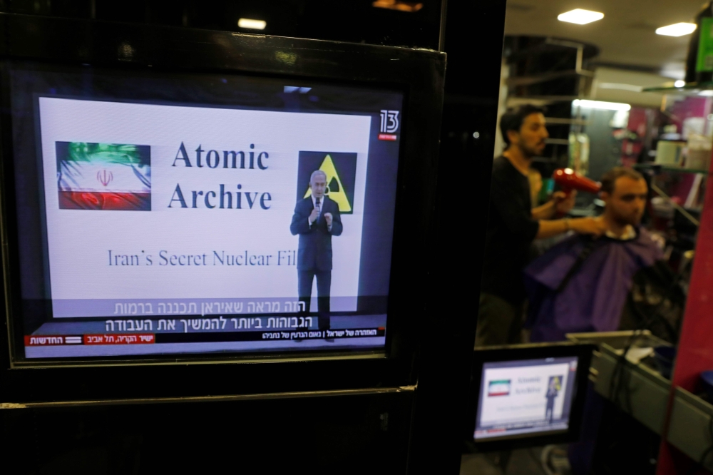 A hairdresser cuts a customer's hairs as Israeli prime minister's speech on Iran's nuclear program is broadcasted on televisions in Jerusalem on April 30, 2018.  AFP / Menahem KAHANA
