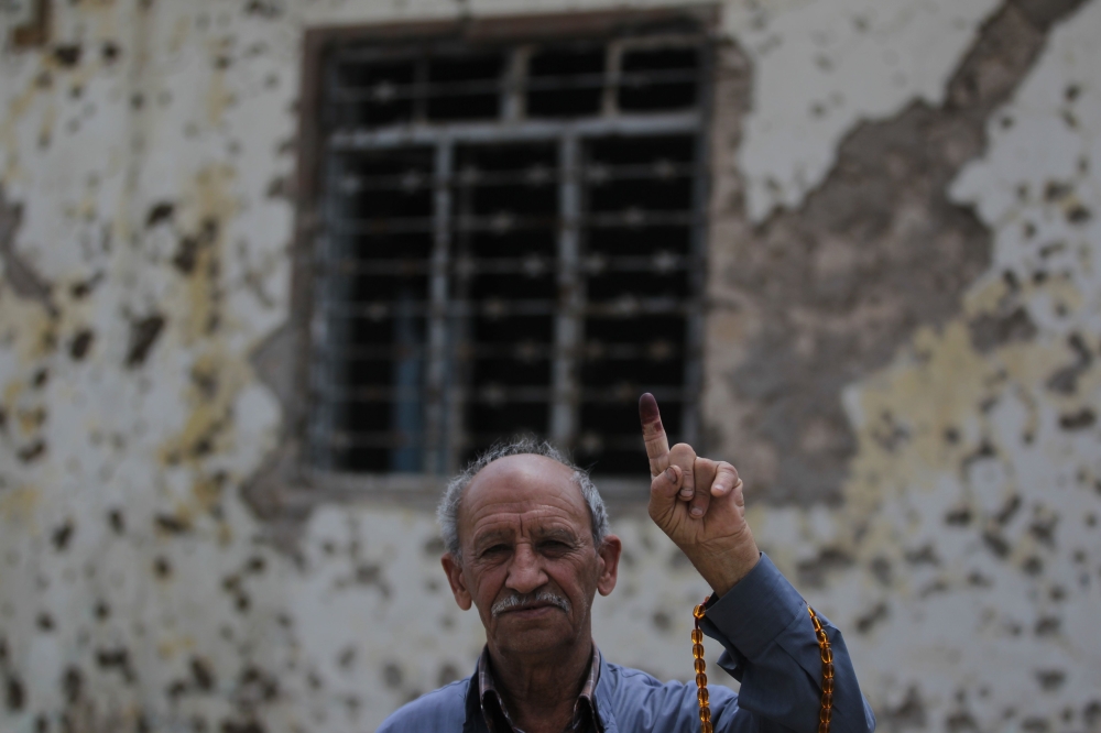 An Iraqi voter shows his ink-stained index finger in front of a damaged wall in western Mosul's Zanjili neighbourhood on May 12, 2018, still partially in ruins from the devastating months-long fight to oust the Islamic State (IS) group.   AFP / AHMAD AL-R