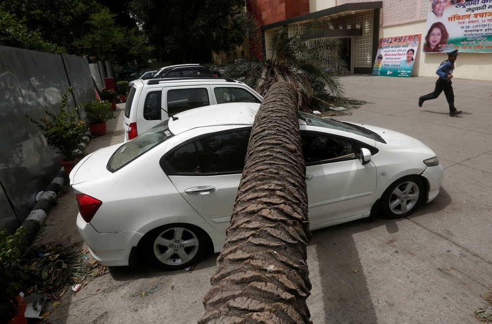 A security guard runs past cars damaged by a fallen tree after Sunday night's dust storm in New Delhi, India May 14, 2018. REUTERS/Adnan Abidi