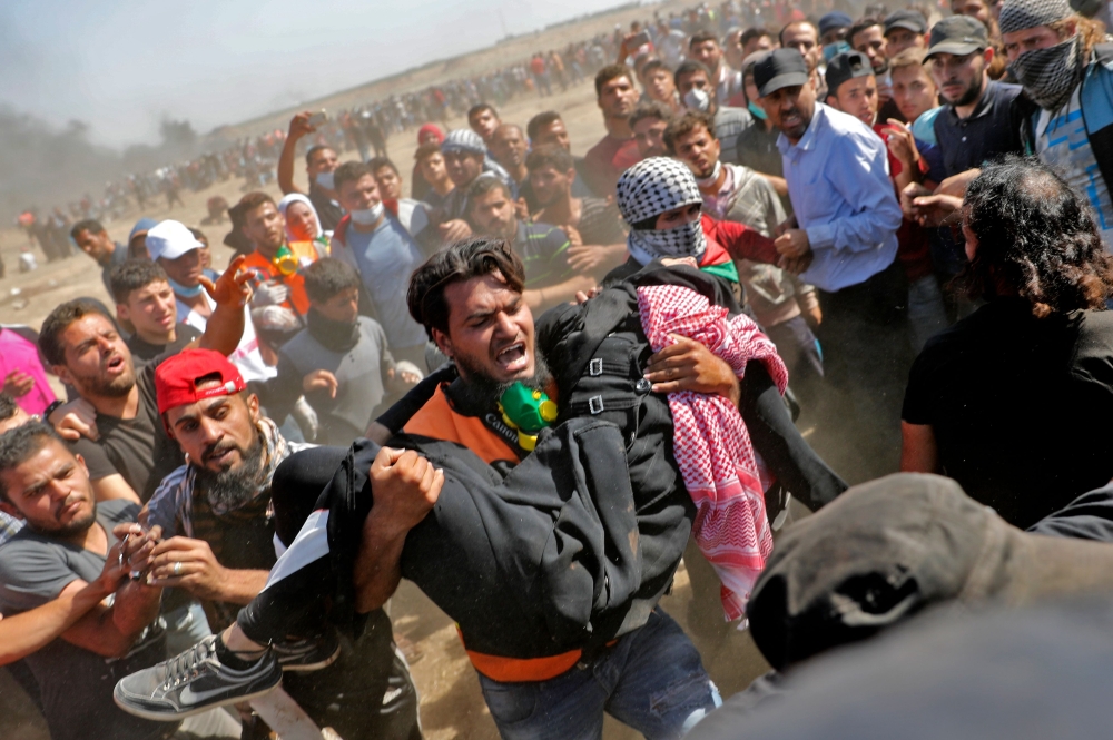 Palestinians carry a demonstrator injured during clashes with Israeli forces near the border between the Gaza strip and Israel east of Gaza City on May 14, 2018, as Palestinians protest over the inauguration of the US embassy following its controversial m