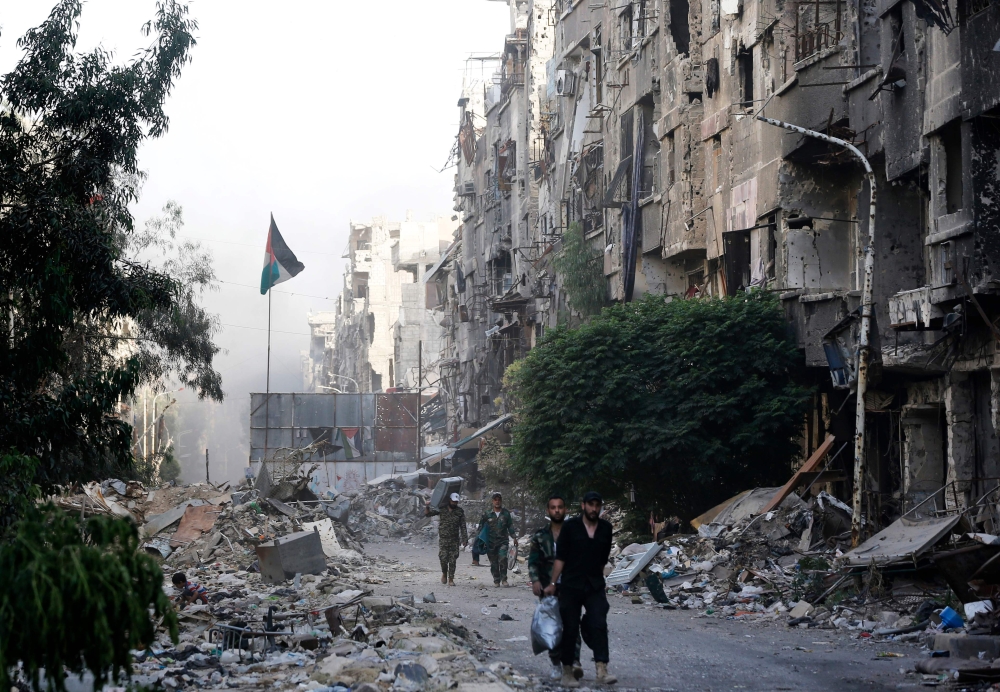 Syrian government forces walk down a destroyed street in the Palestinian camp of Yarmuk on the southern outskirts of Damascus on May 21, 2018. AFP / LOUAI BESHARA