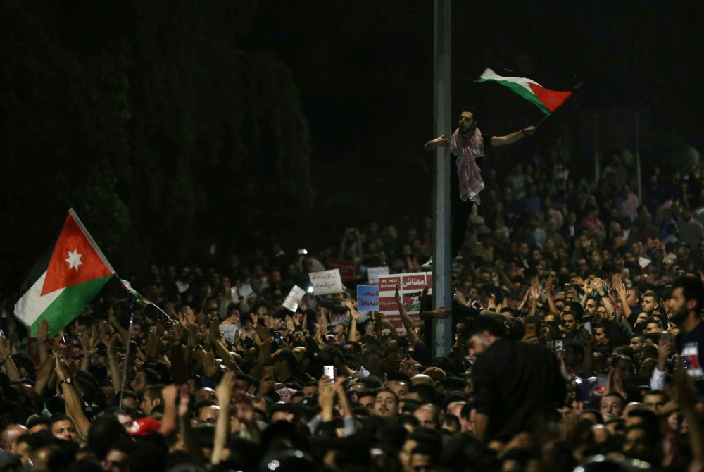 Protesters wave flags near Jordanian security forces during a demonstration outside the prime minister's office in the capital Amman late on June 3, 2018.  AFP / Khalil MAZRAAWI
