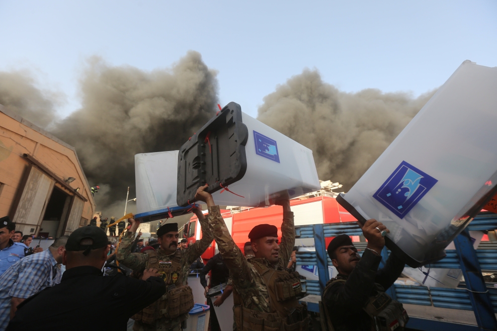Security forces carry ballot boxes as smoke rises from a storage site in Baghdad, housing the boxes from Iraq's May parliamentary election, Iraq June 10, 2018. Reuters
