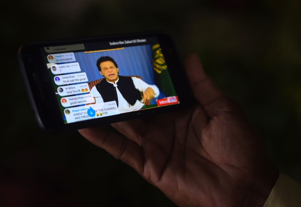 A Pakistani man holds his smartphone, as he watches a broadcast of a speech of newly appointed Pakistani Prime Minister Imran Khan, as he addresses the nation, in Karachi on August 19, 2018. (AFP / RIZWAN TABASSUM)