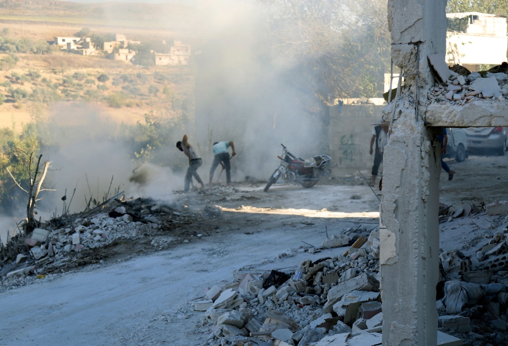 Syrians use dirt to put out a fire at the scene of a reported air strike in the district of Jisr al-Shughur, in the Idlib province, on September 4, 2018. AFP / Zein Al Rifai