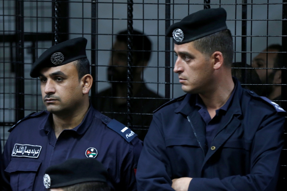 The accused look on behind police officers during their trail for staging an attack on December 2016 on a Crusader castle in Kerak, at the State Security Court, in Amman, Jordan November 13, 2018. REUTERS/Muhammad Hamed