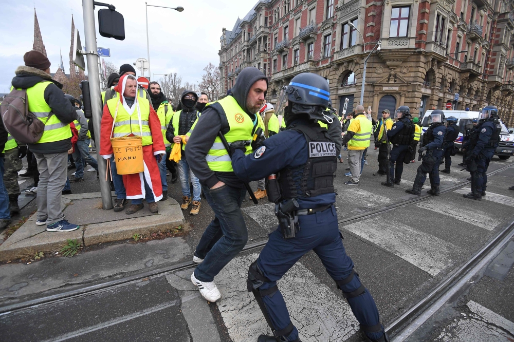 Demonstrators face riot police officers during a protest of Yellow vests (Gilets jaunes) against rising oil prices and living costs, in Strasbourg, eastern France, on December 1, 2018. / AFP / PATRICK HERTZOG