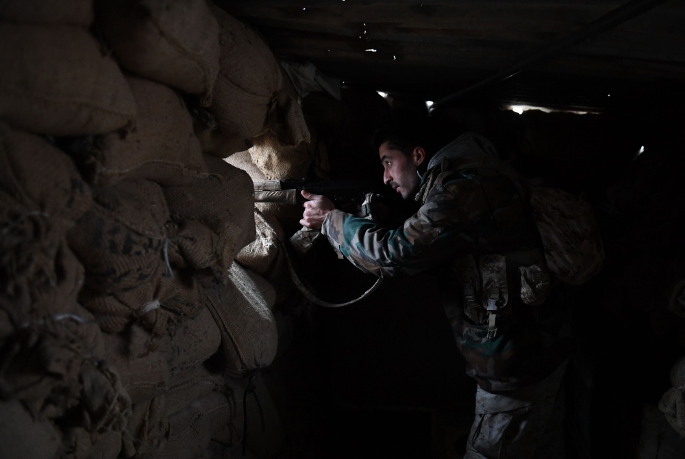 A member of the Syrian regime forces watches through the opening of a sandbag barricade in the southern countryside of the northern Kurdish-controlled city of Manbij on December 30, 2018.   AFP 
