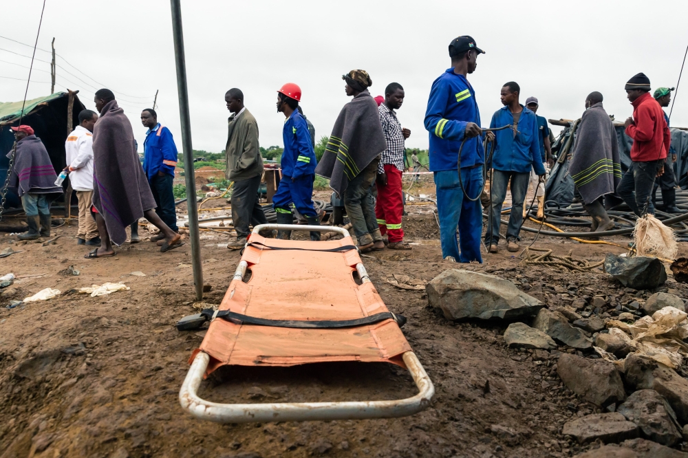 Men walk past a stretcher during an ongoing rescue and recovery operation at the flooded Cricket gold mine near Kadoma, Zimbabwe, on February 17, 2019.   AFP / Jekesai NJIKIZANA