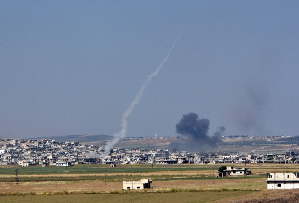 Smoke from an incoming shell (R) billows above buildings in the town of Kafr Nabuda as a rocket fired from the twon leaves a white trace of smoke, in the north of the Syrian Hama province during reported air strikes by Syrian regime forces on May 26, 2018