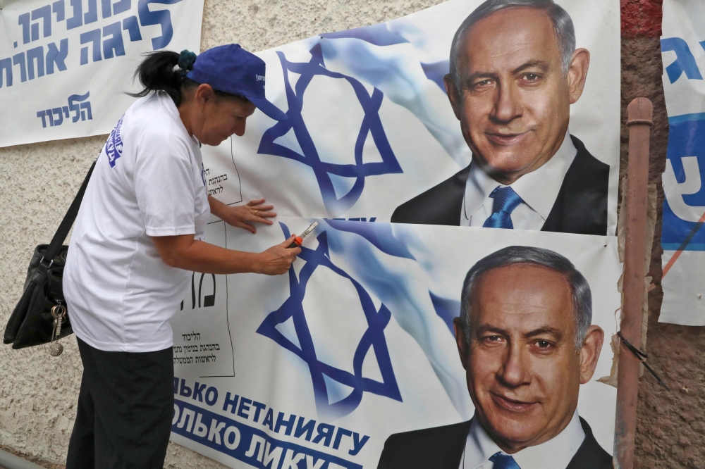A woman places electoral banners for the Likud party showing Benjamin Netanyahu in the southern Israeli city of Beersheva on September 15, 2019. AFP/Hazem Bader