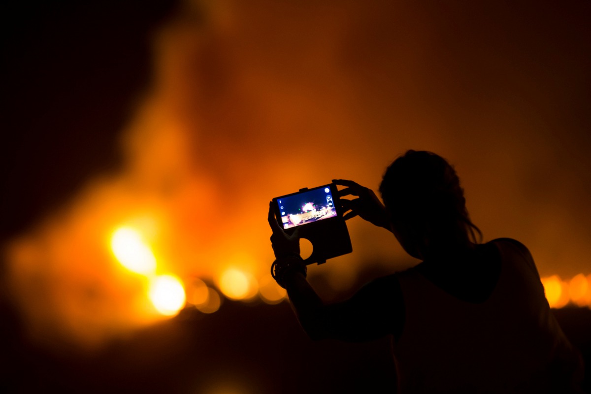 A woman uses her mobile phone to film as a forest fire burns out of control in Las Manchas on the southwestern part of La Palma island, Spain, early August 5. 2016. Reuters / Borja Suarez