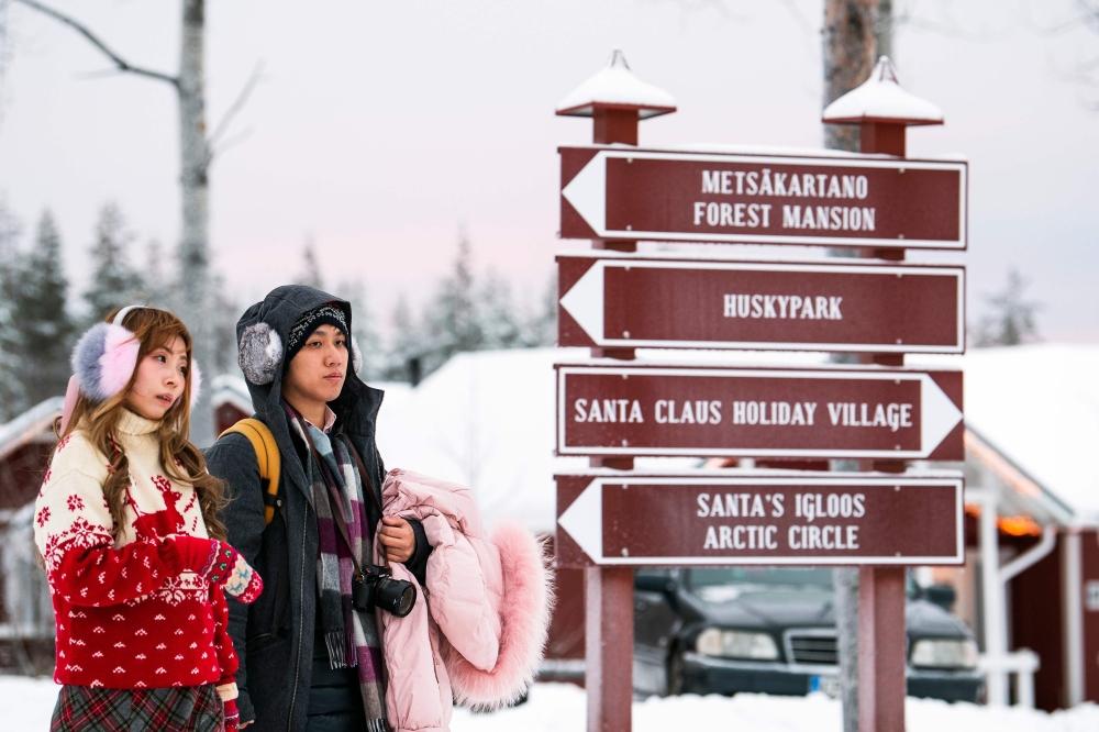 Tourists look at information boards during their visit to the Santa Claus Village near Rovaniemi, Finnish Lapland, on December 2, 2019. AFP / Jonathan Nackstrand