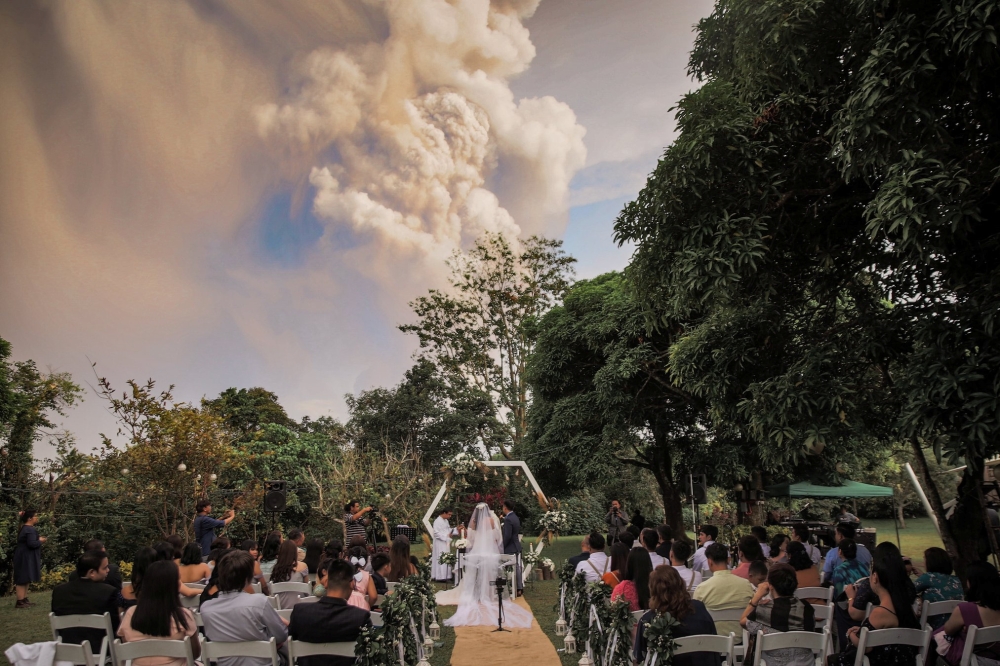 People attend a wedding ceremony as Taal Volcano sends out a column of ash in the background in Alfonso, Cavite, Philippines, January 12, 2020, in this image obtained from social media. Courtesy of Randolf Evan Photography/Social Media via REUTERS