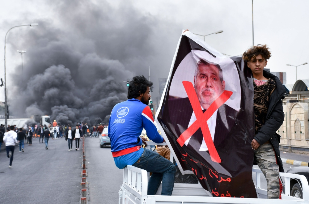 Iraqi demonstrators lift a poster of premier-designate Mohammad Allawi with the mention 