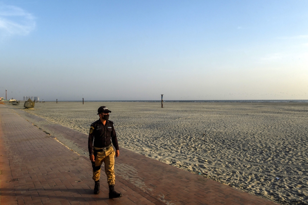 A policeman wearing a facemask patrols at the deserted Clifton beach after a public ban imposed by the national authorities amid concerns over the spread of the COVID-19 novel coronavirus, in Karachi on March 18, 2020. / AFP / Asif HASSAN