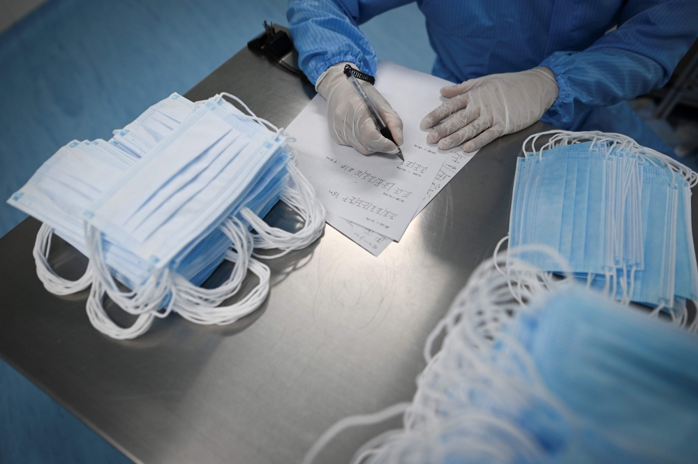 A worker wearing a protective suit counts masks at Naton Medical Group, a company which makes medical equipment in Beijing on April 24, 2020.  AFP / WANG ZHAO
