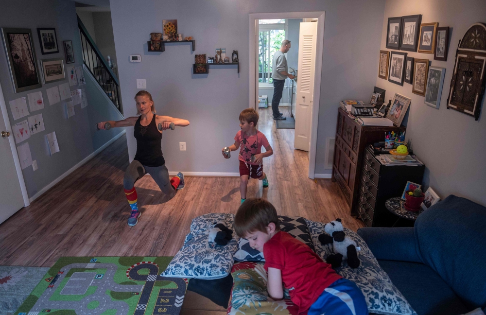 Mimicked by her son Daniel (R), Paulina Mansz, a group fitness instructor, records a workout session for her clients while her other son Javier relaxes and her husband Manuel cooks in the kitchen, as she continues to instruct from home in Arlington, Virgi