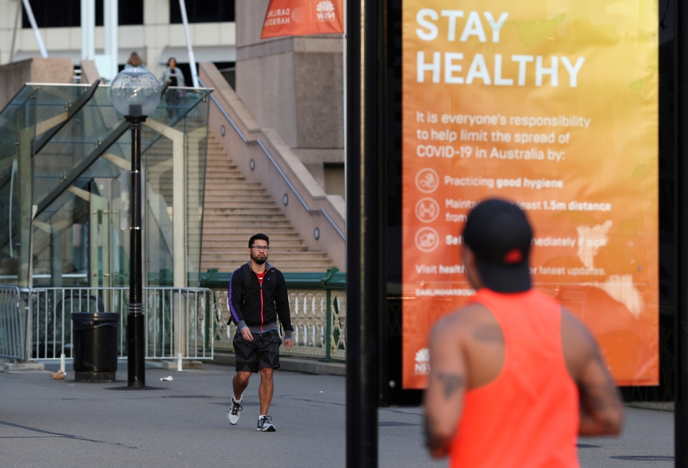 FILE PHOTO: A man walks near an info board following the easing of restrictions implemented to curb the spread of the coronavirus disease (COVID-19), at Darling Harbour near the city centre in Sydney, Australia, May 18, 2020. REUTERS/Loren Elliott/File Ph
