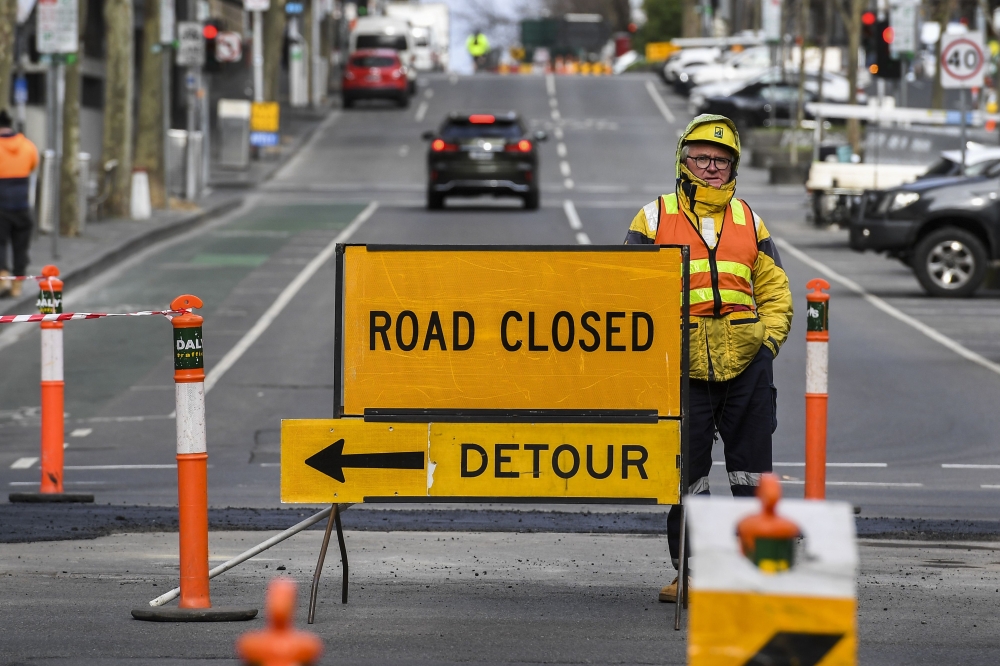A worker stands besides a road sign in Melbourne on July 21, 2020. AFP / William West 