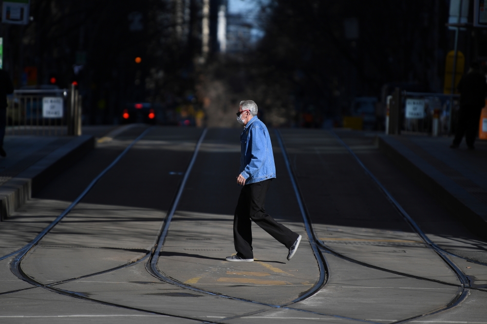 A pedestrian wearing a face mask crosses an empty street as the city operates under lockdown in response to an outbreak of the coronavirus disease (COVID-19) in Melbourne, Australia, August 18, 2020. AAP Image/James Ross via REUTERS 