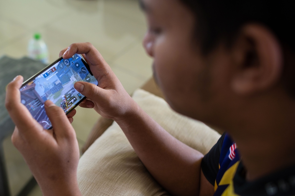 This picture taken on August 22, 2020 shows stateless eSports player Muhammad Aiman Hafizi Ahmad, 20, playing PlayerUnknown's Battlegrounds (PUBG), an online multiplayer gaming on his mobile phone at a house used by his gaming team in Bangi town, south of