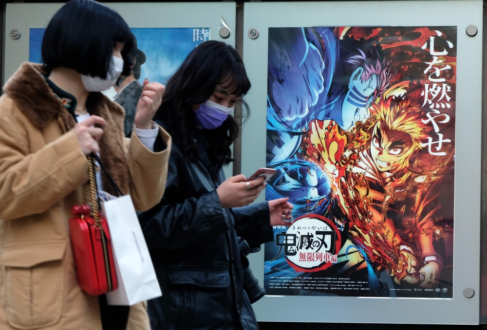 In this picture taken on December 16, 2020, pedestrians walk past a poster promoting the anime movie Demon Slayer -- Kimetsu no Yaiba the Movie: Mugen Train -- at a cinema in Tokyo. An anime epic in which a teenager hunts down and beheads demons has becom