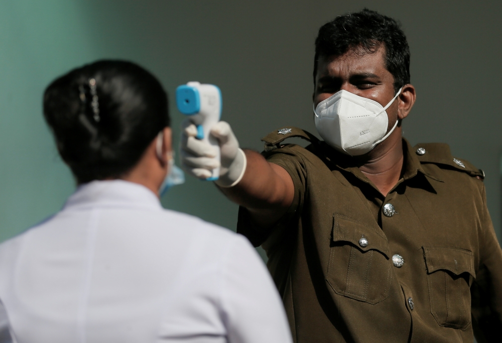 A health official uses a thermometer to take the temperature of a healthcare worker during a simulation exercise for the coronavirus disease (COVID-19) vaccination in the Piliyandala suburb, south of Colombo, Sri Lanka January 23, 2021.REUTERS/Dinuka Liya