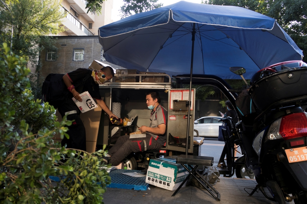  A delivery driver sorts parcels as he sits in the trunk of his electric tricycle following an outbreak of the coronavirus disease (COVID-19) in Beijing, China, August 21, 2020. REUTERS/Thomas Peter/File Photo