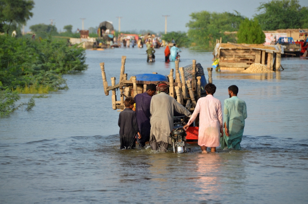 Men walk along a flooded road with their belongings, following rains and floods during the monsoon season in Sohbatpur, Pakistan, August 28, 2022. (REUTERS/Amer Hussain)
