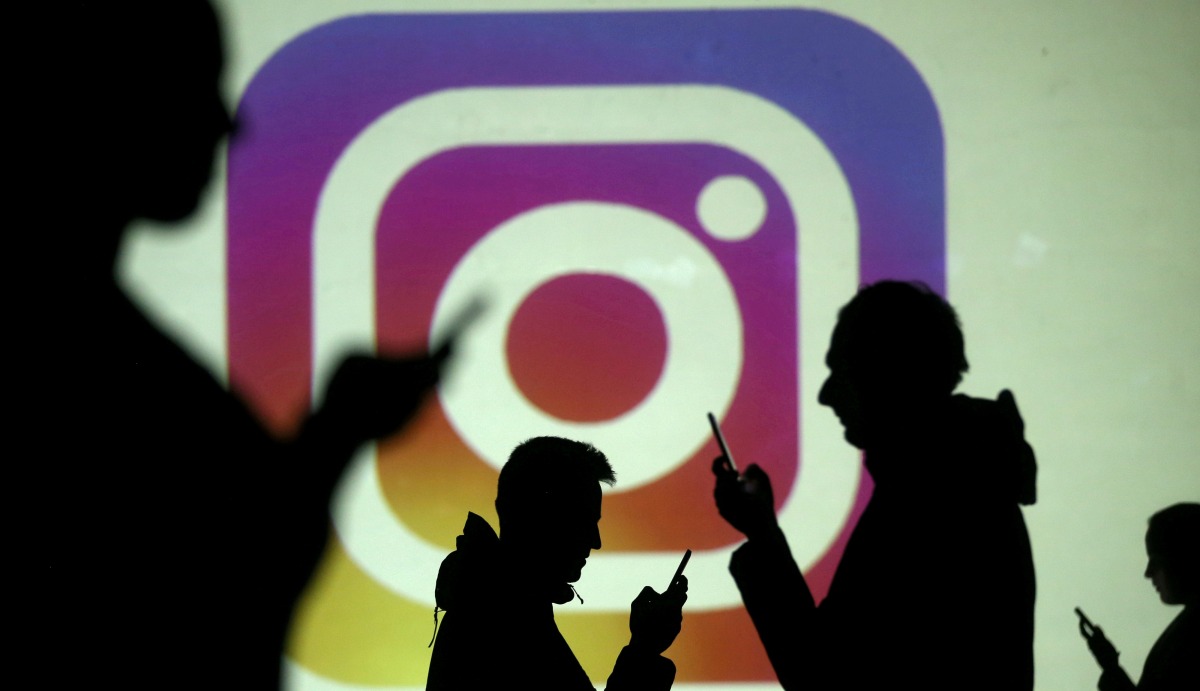 Silhouettes of mobile users are seen next to a screen projection of the Instagram logo in this picture illustration taken on March 28, 2018. File Photo / Reuters
