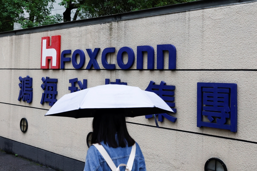 A woman carrying an umbrella walks past the logo of Foxconn outside a company's building in Taipei, Taiwan October 31, 2022. REUTERS/Carlos Garcia Rawlins