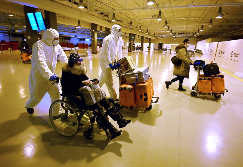 Workers wearing protective masks and suits help Chinese travellers leaving the arrival hall of Rome's Fiumicino International Airport on December 29, 2022 after being tested for the Covid-19 coronavirus. (Photo by Filippo Monteforte / AFP)