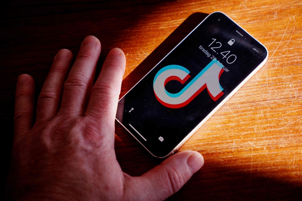 A picture taken on February 28, 2023 in Randers, Denmark shows a hand holding a smartphone with the TikTok app on the screen. - Denmark's parliament announced February 28, 2023 that it had asked MPs and all staff to remove the TikTok app from mobile devices because of the 
