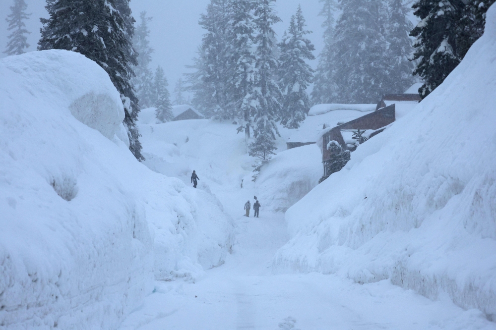 People walk down a street lined by snowbanks piled up from current and previous storms, during another winter storm in the Sierra Nevada mountains, on March 10, 2023 in Mammoth Lakes, California. Mario Tama/Getty Images/AFP 