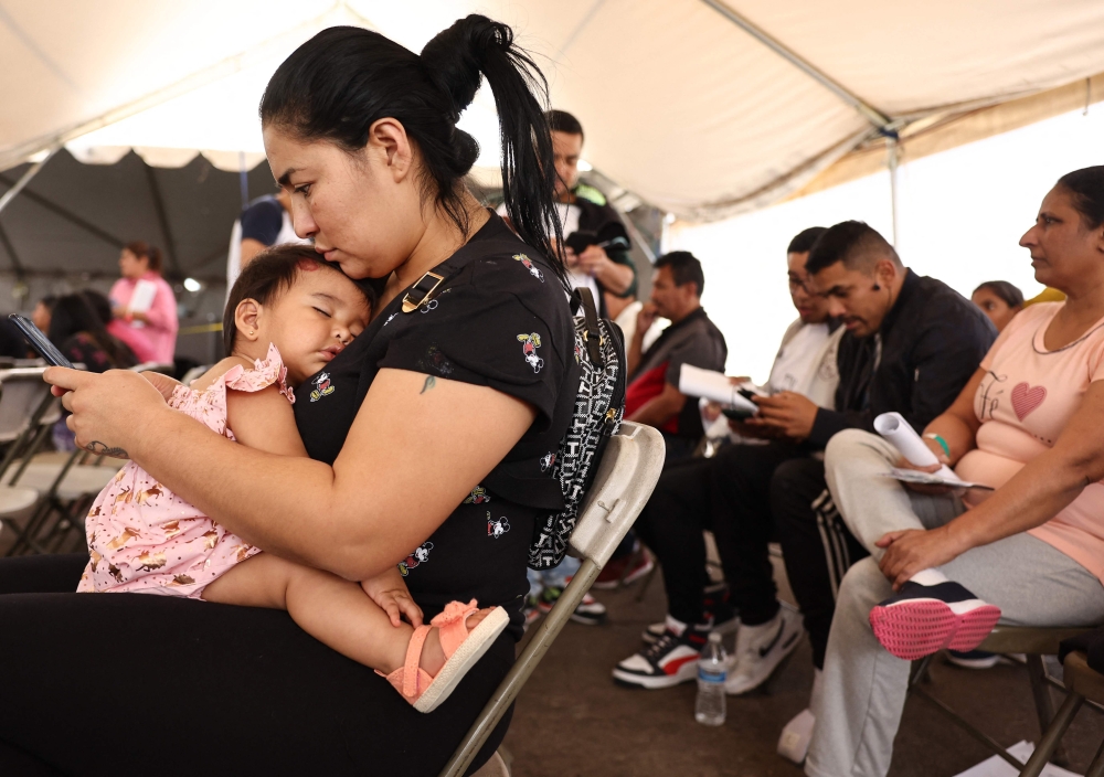 Immigrant mother Andrea, from Ecuador, holds her daughter Mia, nine months, while using her phone at a migrant transition center for asylum seekers released from Border Patrol custody after crossing into the United States, on May 12, 2023 in Somerton, Arizona. (Photo by MARIO TAMA / GETTY IMAGES NORTH AMERICA / Getty Images via AFP)
