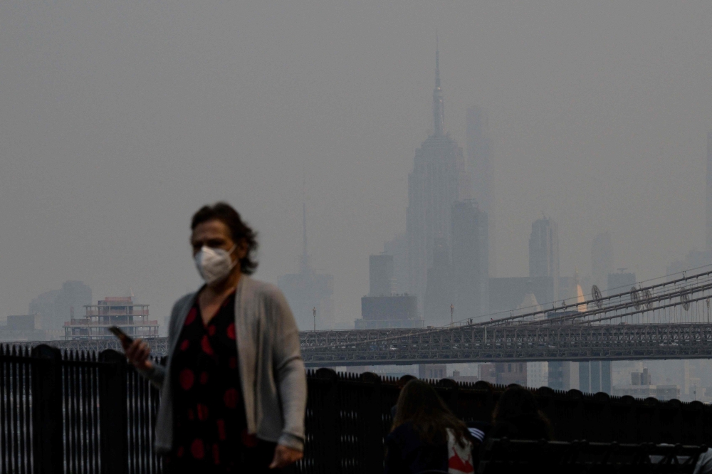 A person wearing a face mask walks before the Empire State Building during heavy smog in New York on June 6, 2023. (Photo by Angela Weiss / AFP)