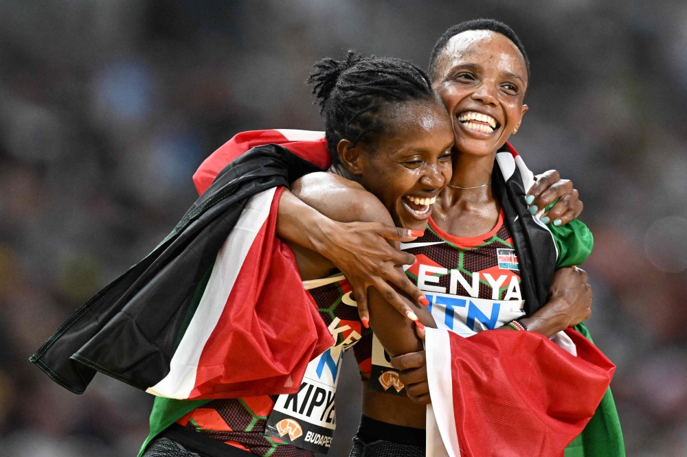 Kenya's Faith Kipyegon (L) and Beatrice Chebet celebrate while draped in their national flag after the women's 5000m final during the World Athletics Championships at the National Athletics Centre in Budapest on August 26, 2023. (Photo by Jewel SAMAD / AFP)