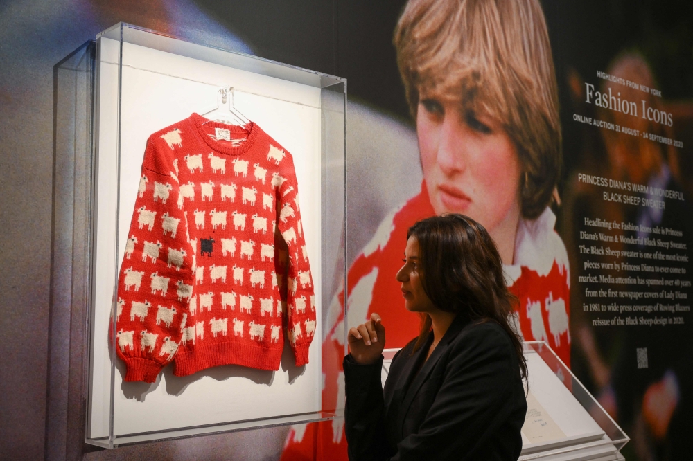 A staff member poses with the 'Black Sheep Jumper' designed by Sally Muir and Joanna Osborne and worn on several occasions by Britain's late Princess Diana, during a press view at Sotheby's auction house in London on July 17, 2023. (Photo by Daniel LEAL / AFP)