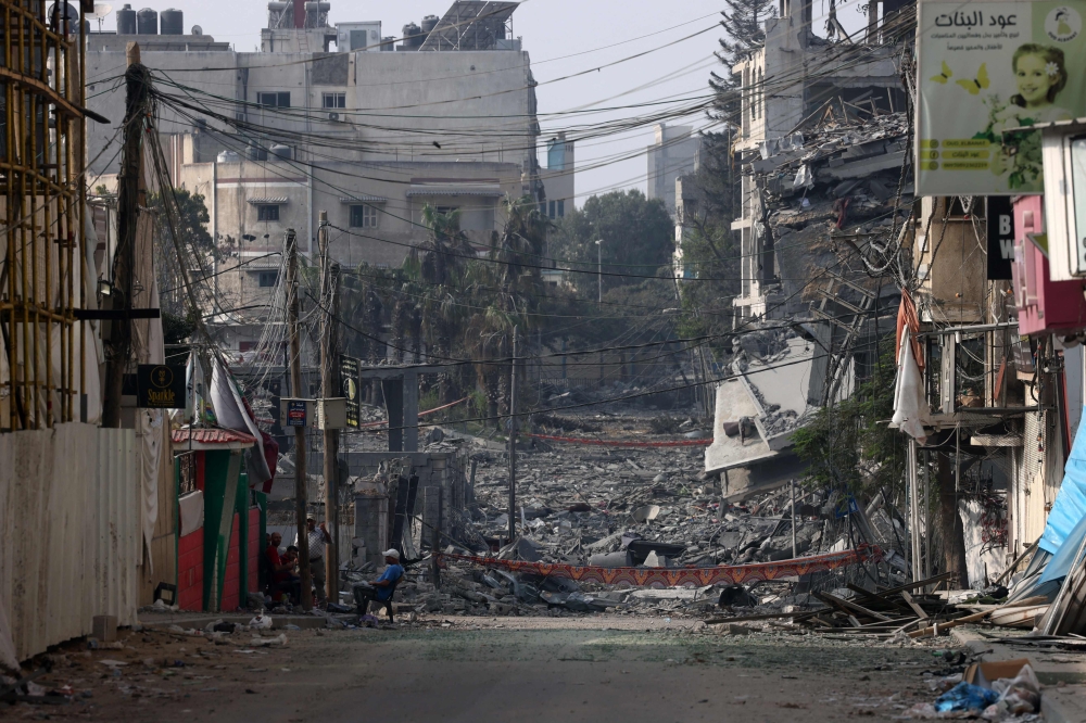 A man sits in front of buildings destroyed by Israeli strikes in Gaza City on October 28, 2023. Photo by MOHAMMED ABED / AFP