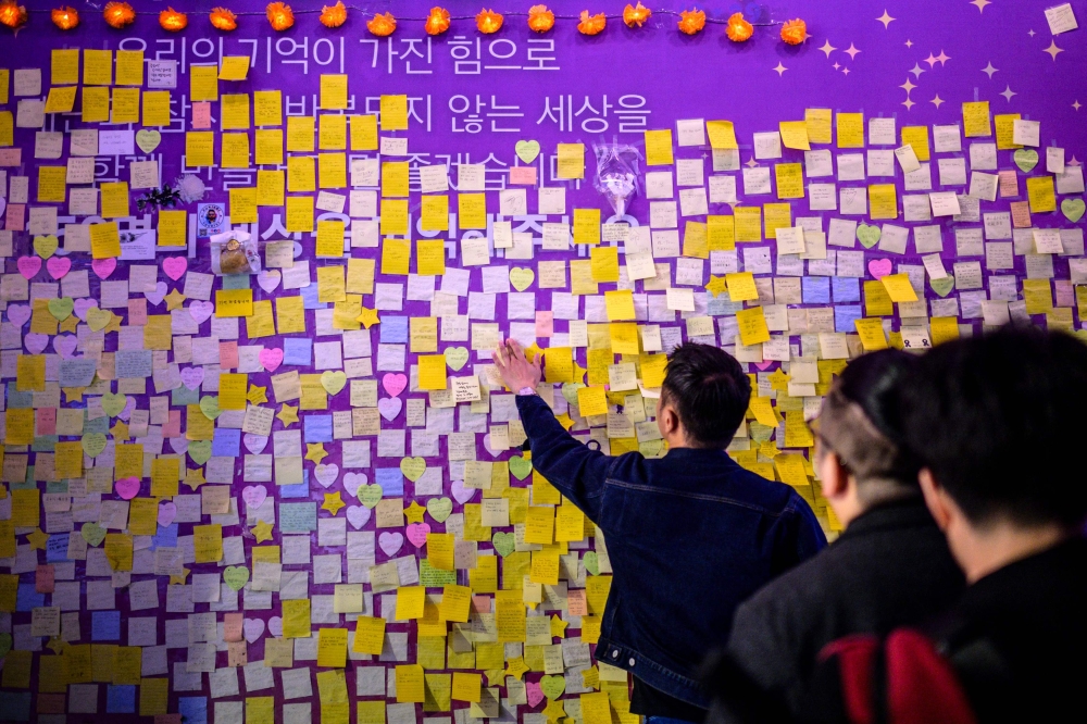 A bystander attaches a handwritten note next to others left on a wall in an alleyway in Seoul late October 28, 2023, which was the site of the October 29, 2022, tragic crowd crush that killed 159 people during Halloween celebrations, in Seoul's popular Itaewon nightlife area. (Photo by ANTHONY WALLACE / AFP)