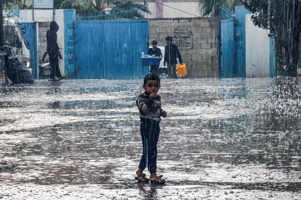 A boy stands in the rain at a school run by the United Nations Relief and Works Agency for Palestine Refugees in the Near East (UNRWA) in Rafah in the southern Gaza Strip on November 14, 2023. Photo by SAID KHATIB / AFP