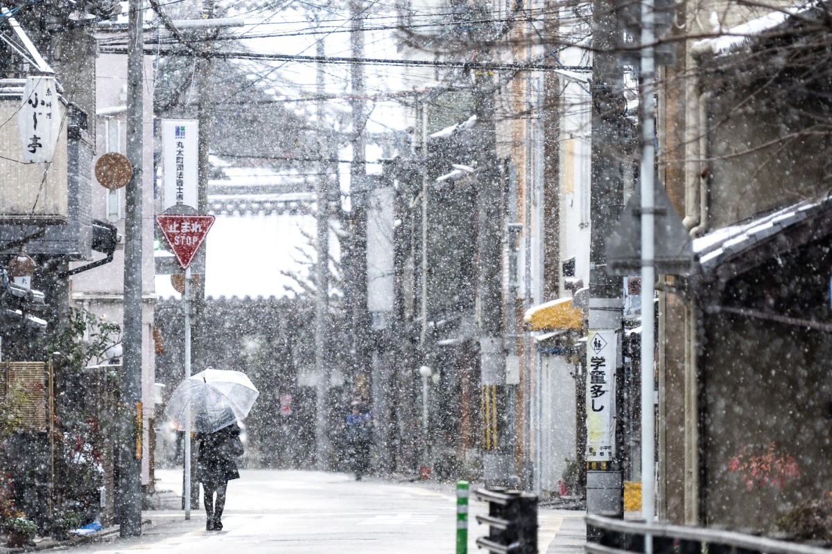 A woman walks on the street as it snows in Kyoto on January 25, 2024. (Photo by Philip FONG / AFP)
